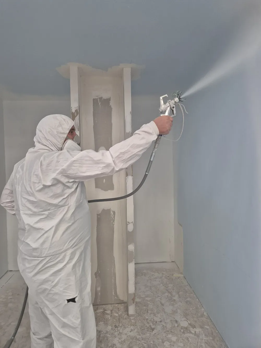 Un homme en combinaison blanche pulvérise de la peinture sur un mur